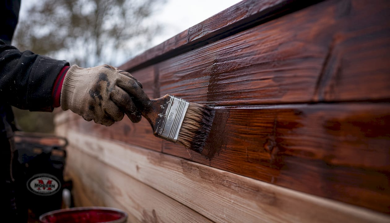 Close-up of hands staining wooden fence