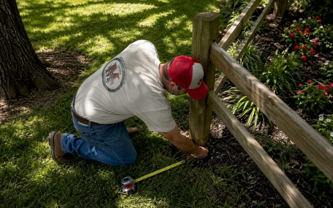 Man inspecting wooden fence post base outdoors