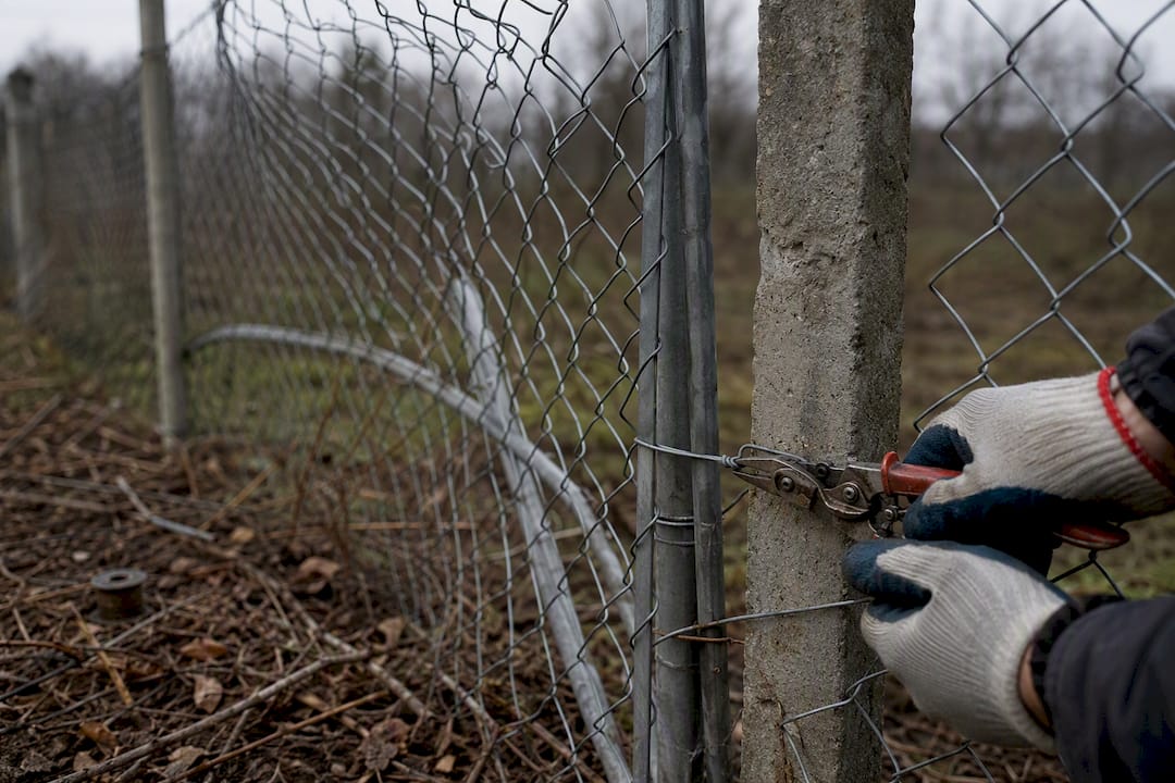 Hands adjusting chain-link fence tension wire